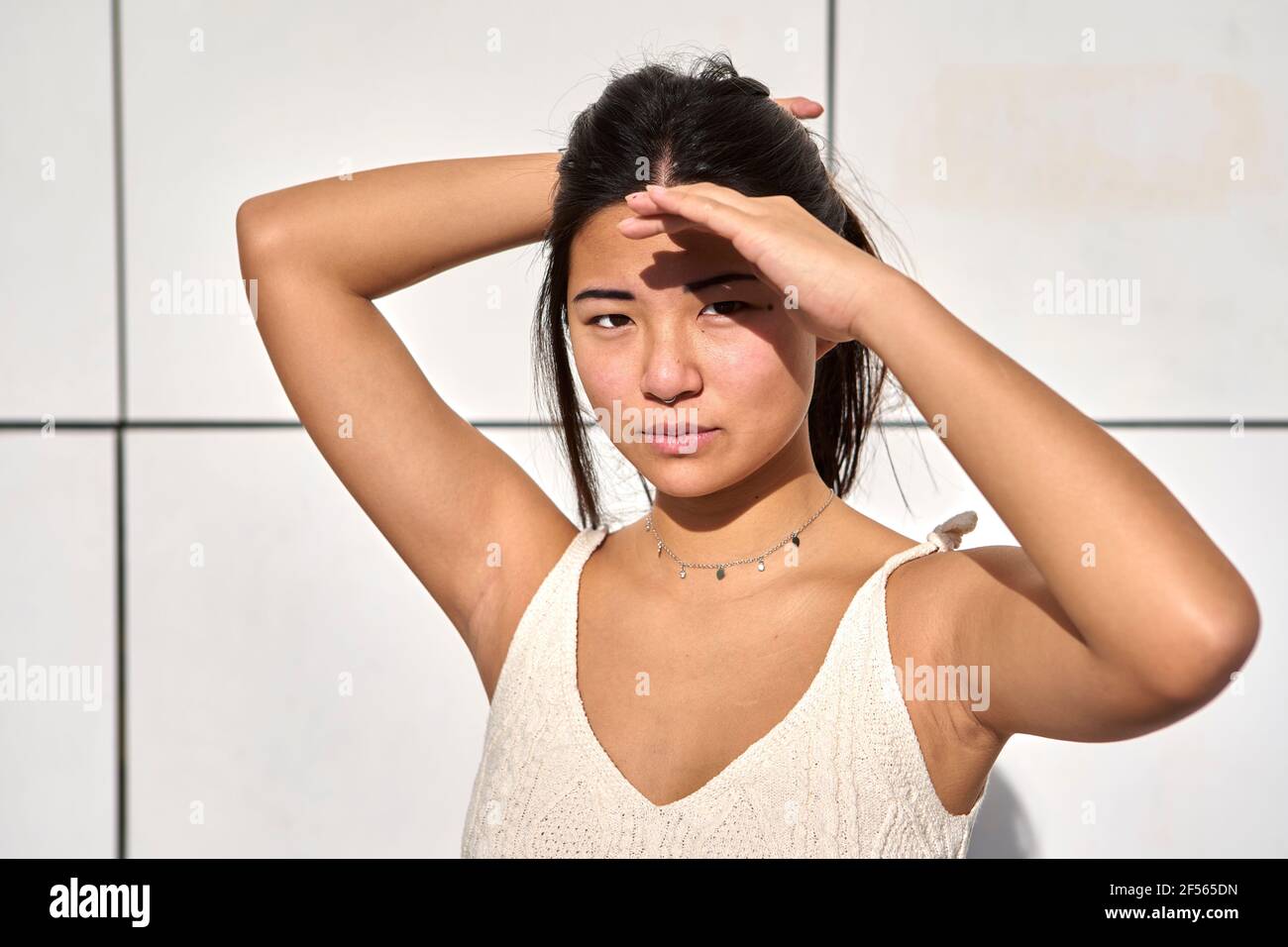 Donna giovane scherma gli occhi per proteggere dalla luce solare contro le pareti Foto Stock