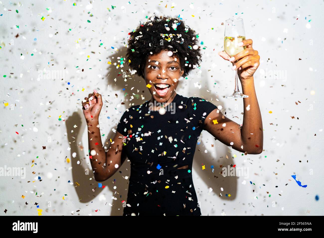 Donna felice con flauto di champagne ballare in piedi tra i confetti su sfondo bianco Foto Stock