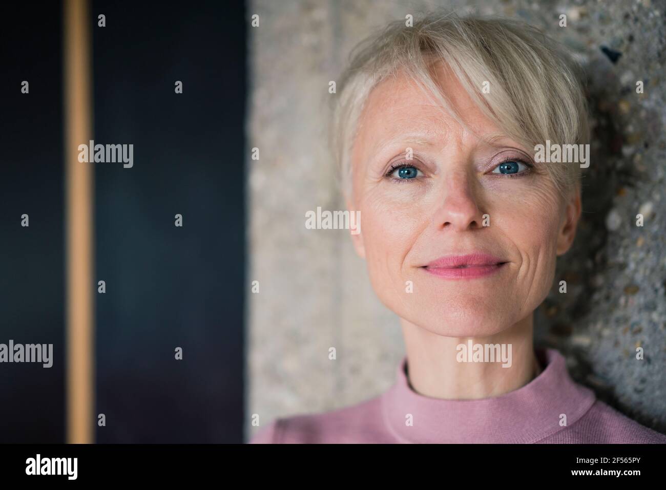 Donna sorridente con occhi blu contro colonna Foto Stock