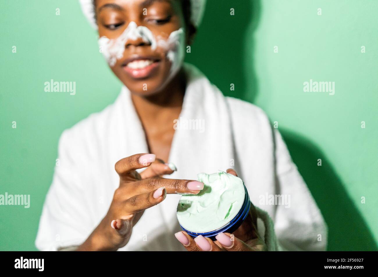 Donna che usa il prodotto di bellezza mentre sta in piedi contro sfondo verde Foto Stock