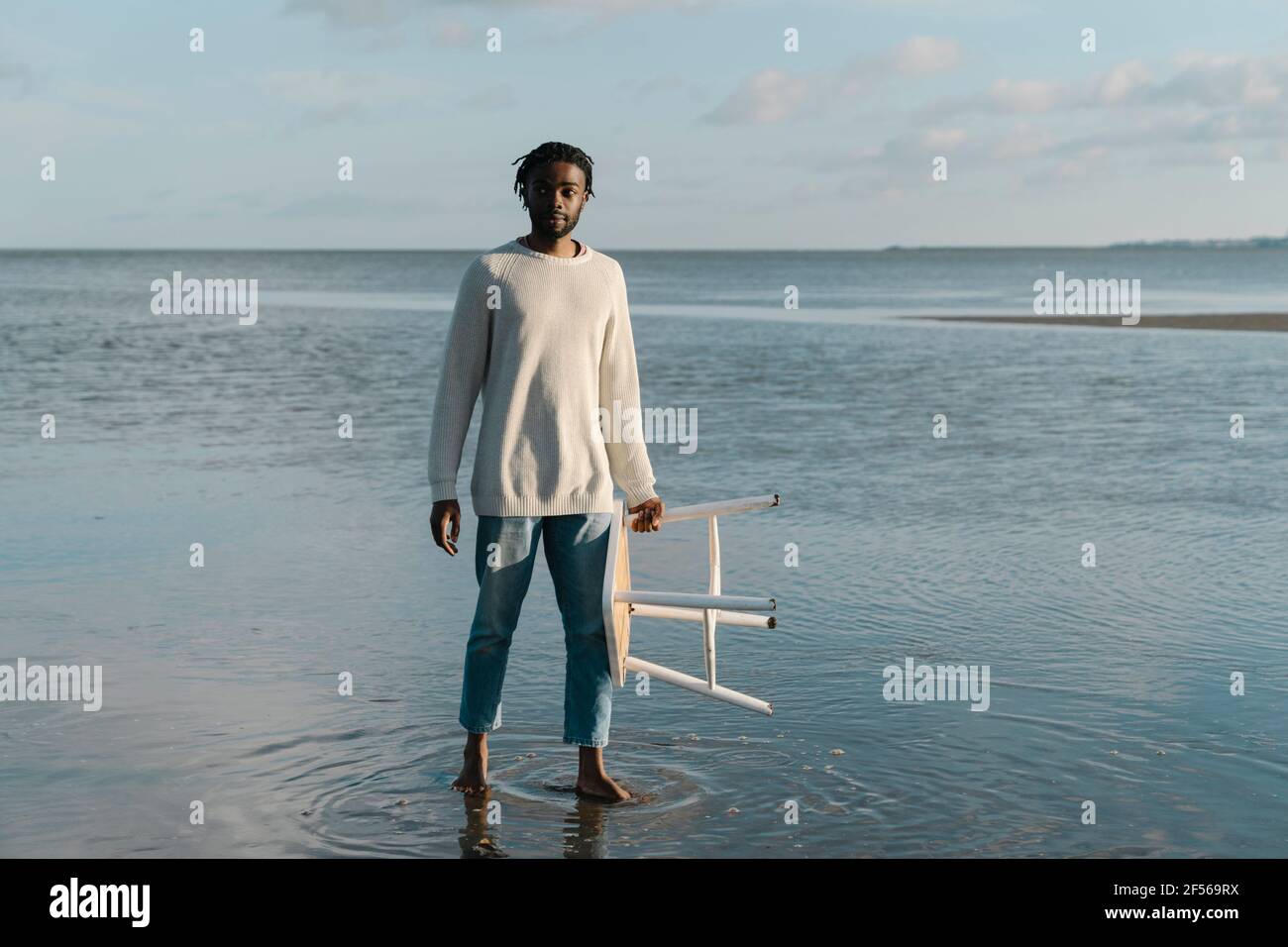 Giovane uomo con sgabello bianco in piedi sulla spiaggia contro il cielo  Foto stock - Alamy