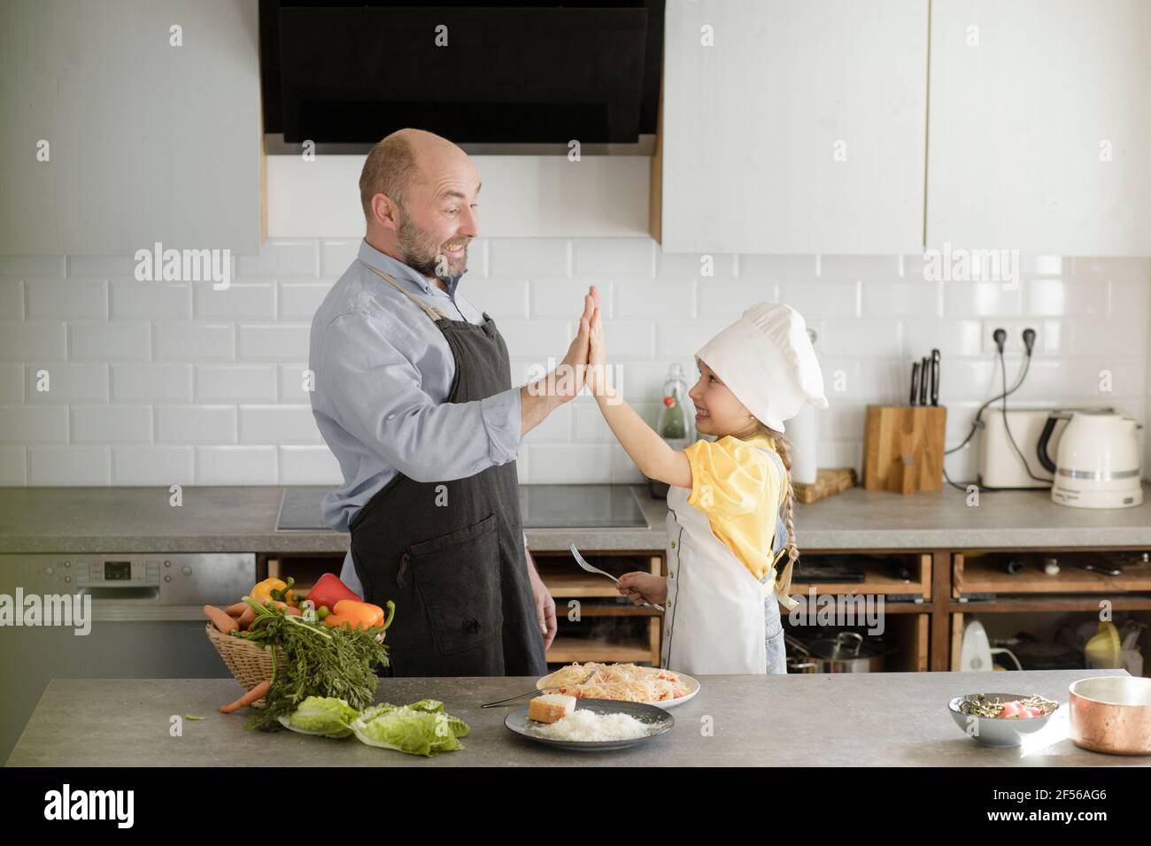 Gli uomini maturi e la ragazza che rallegrano con dare high-five mentre si levano in piedi in cucina a casa Foto Stock