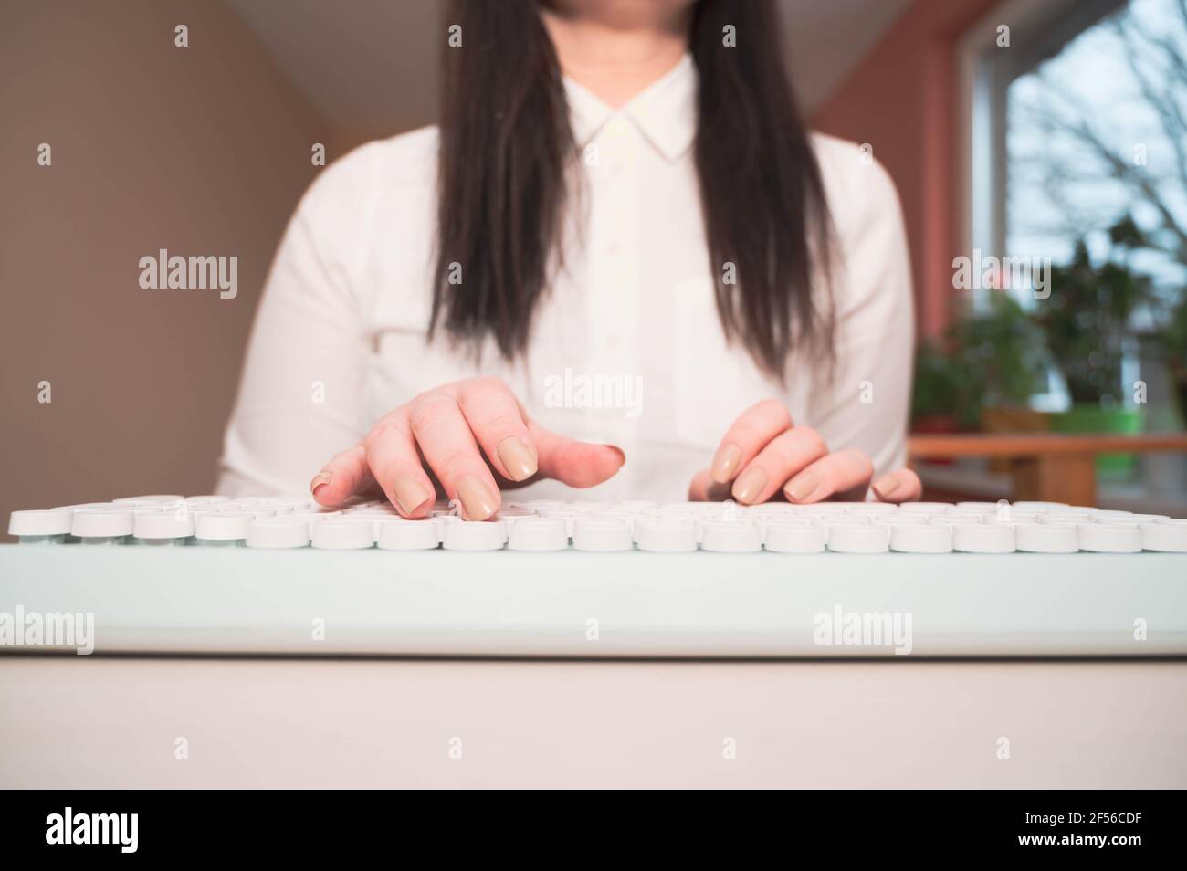 Primo piano donna che scrive su tastiera bianca. Lavorare in remoto da casa Foto Stock