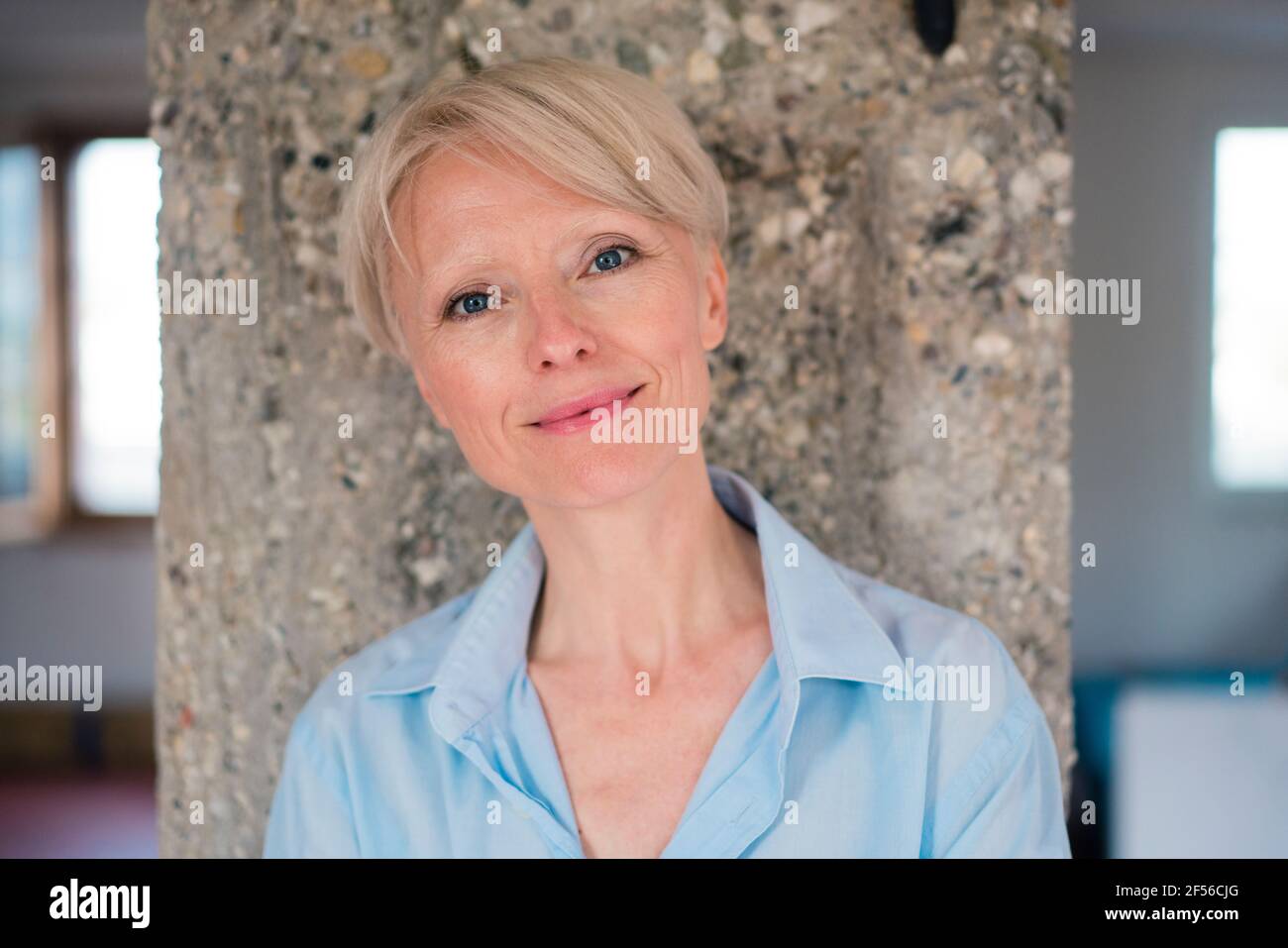 Donna d'affari sorridente con gli occhi blu contro la colonna a casa Foto Stock