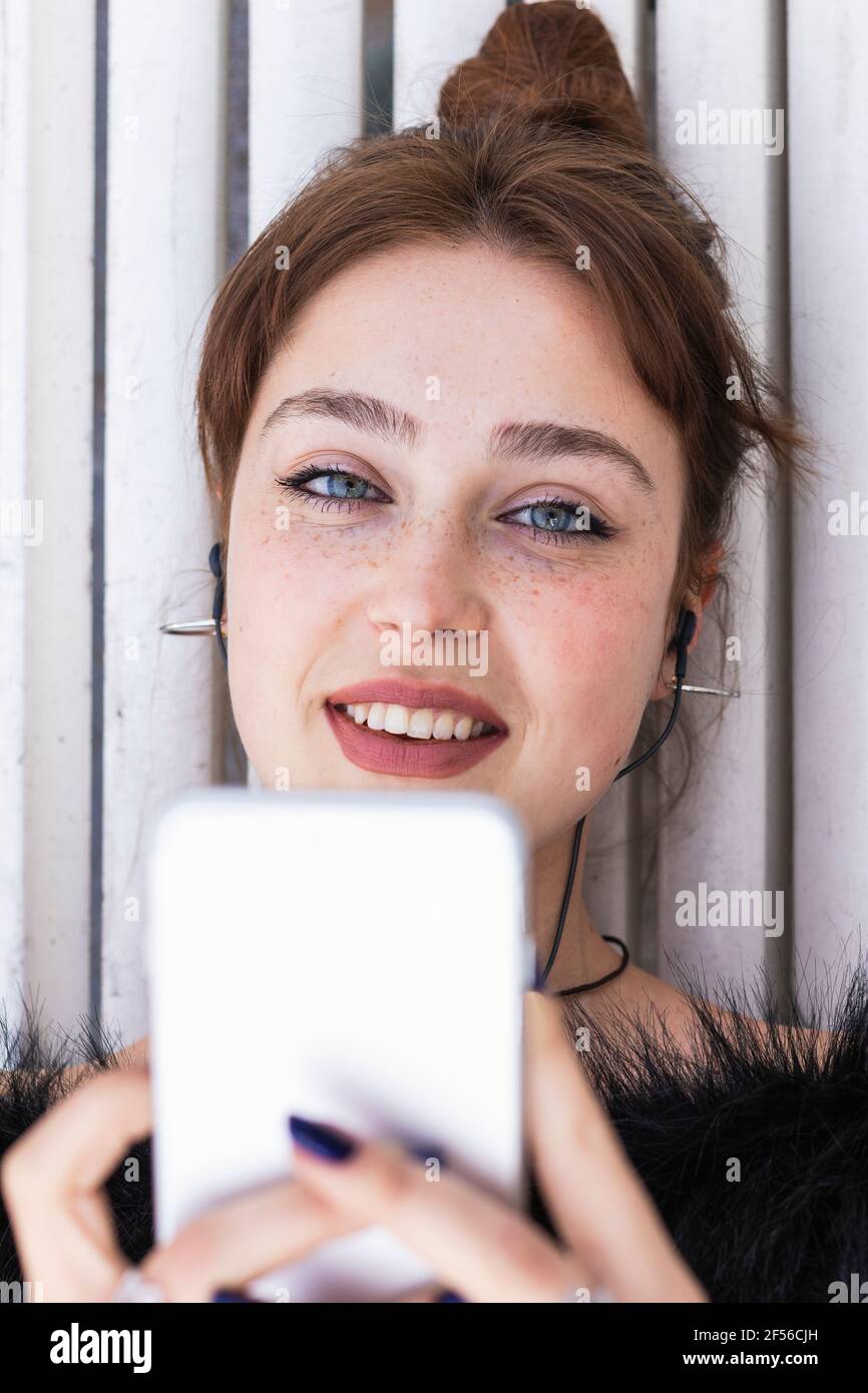 Bella donna con gli occhi blu che tengono lo smartphone durante l'ascolto musica sul banco Foto Stock