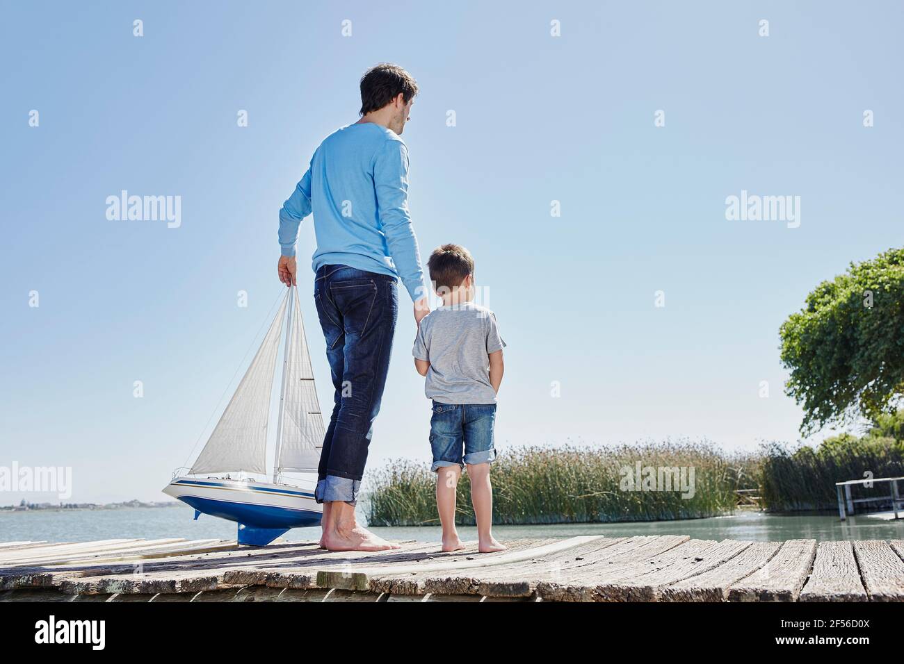 Uomo maturo con la barca a vela giocattolo che tiene la mano di ragazzo mentre in piedi contro il cielo Foto Stock