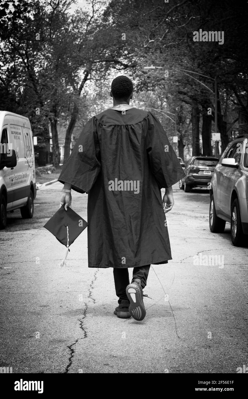 CHICAGO, ILLINOIS. USA 20 MAGGIO 2020: DURANTE L'ALTEZZA DI COVID-19 UN GIOVANE LAUREATO AFRICANO AMERICANO MASCHIO CAMMINA ATTRAVERSO LA STRADA NELL'AREA DI WEST PULLMAN Foto Stock
