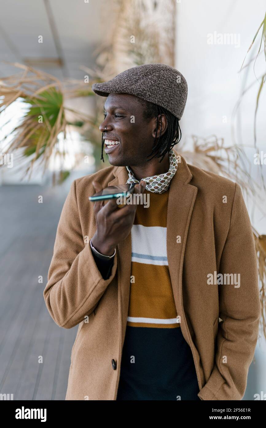 Uomo sorridente in berretto piatto che parla con lo smartphone altoparlante Foto Stock