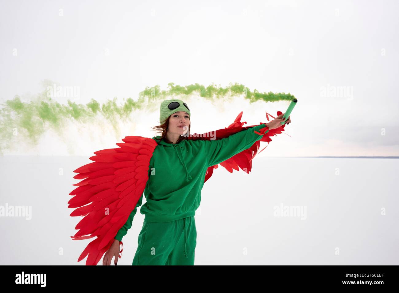 Donna in costume di uccello verde che tiene il flare di distress contro il cielo Foto Stock