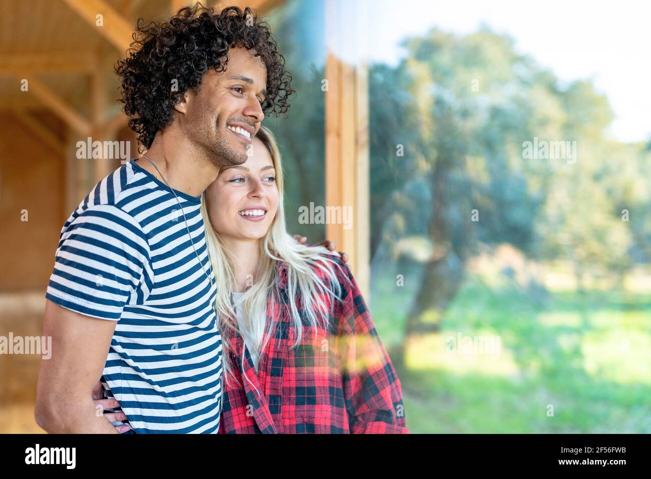 Ragazza sorridente in piedi con braccio intorno al ragazzo dalla finestra a. cortile anteriore Foto Stock