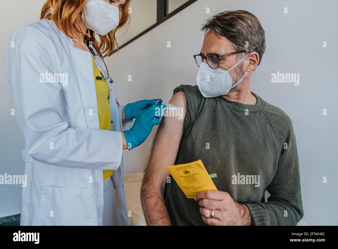 Medico femminile che mette il bendaggio adesivo sul braccio del paziente mentre è in piedi in sala esame Foto Stock