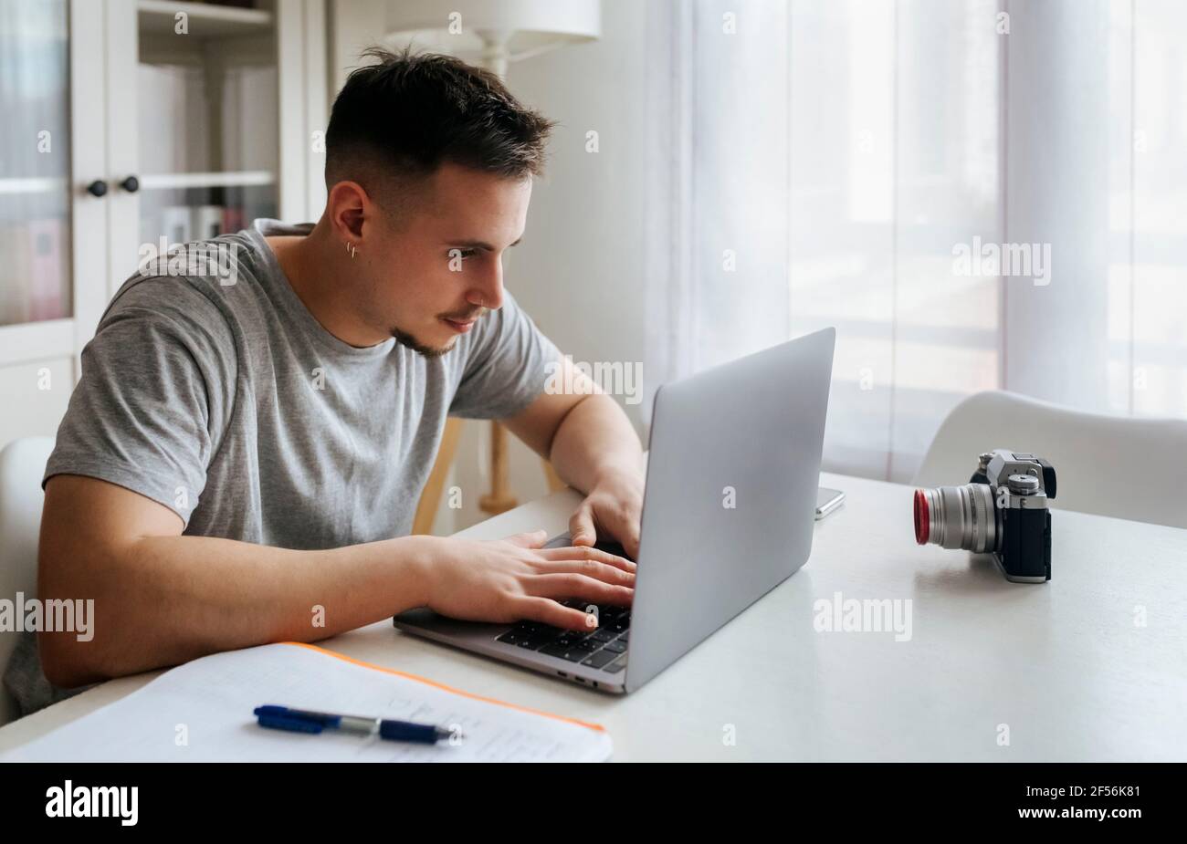 Giovane professionista di sesso maschile che utilizza un computer portatile mentre registra video tramite fotocamera digitale in ufficio Foto Stock