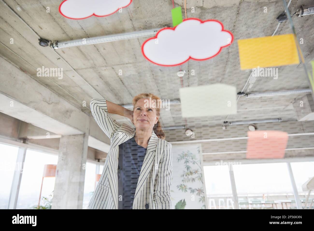 Lavoratore freelance femminile con la mano dietro la testa vista attraverso il vetro mentre si osservano le note adesive in ufficio Foto Stock