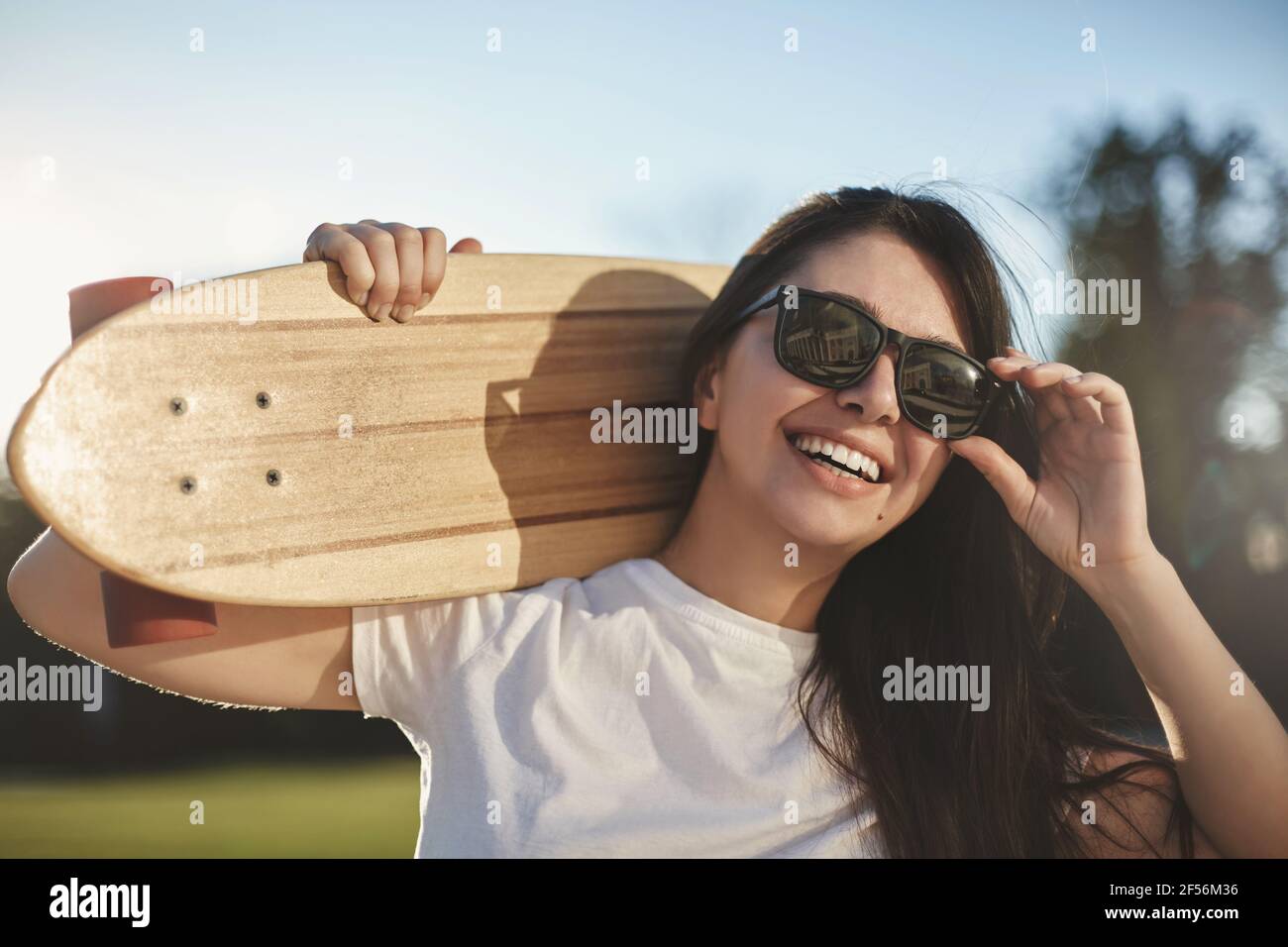 Emozioni, giovani e concetto di skateboard cittadino. Primo piano allegra ragazza skater felice tenere in legno penny bordo sulla spalla, ridendo spensierato toccando Foto Stock