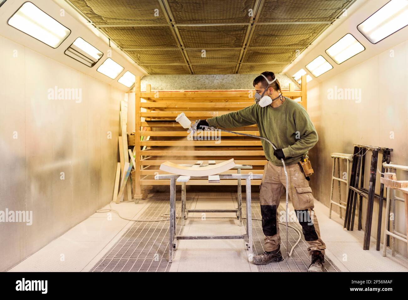 Falegname maschio verniciatura a spruzzo su materiale in legno in cabina di verniciatura Foto Stock
