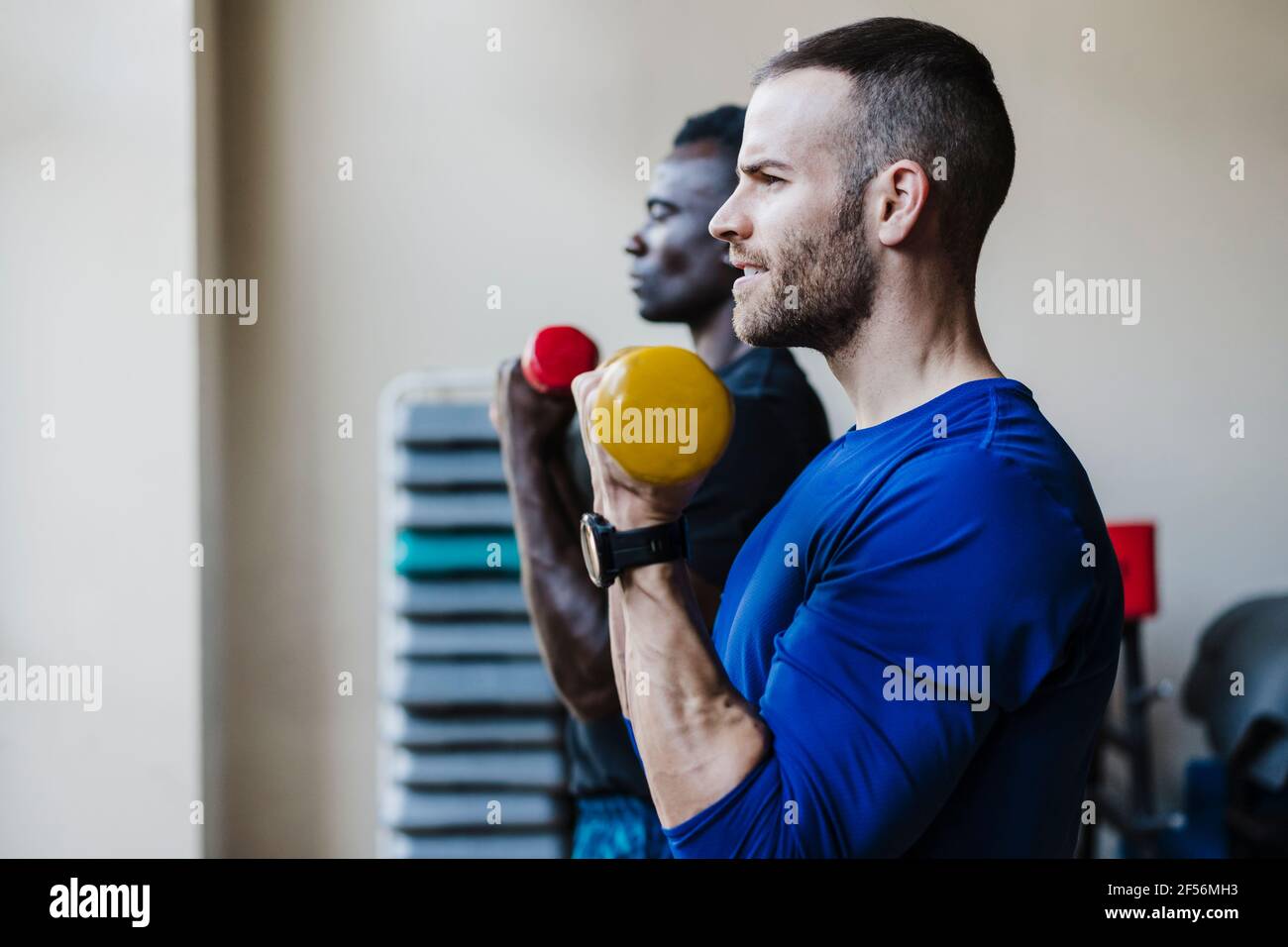 Atleti maschili che si allenano con i manubri durante l'allenamento sportivo in palestra Foto Stock