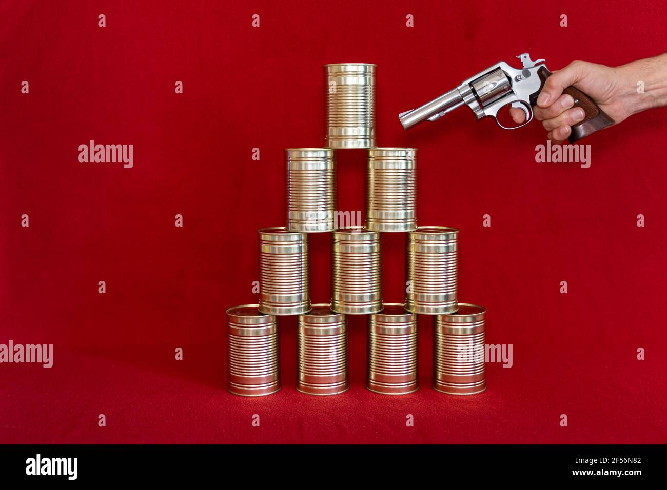 Mano umana che tiene la pistola contro la pila di lattine di stagno Foto Stock