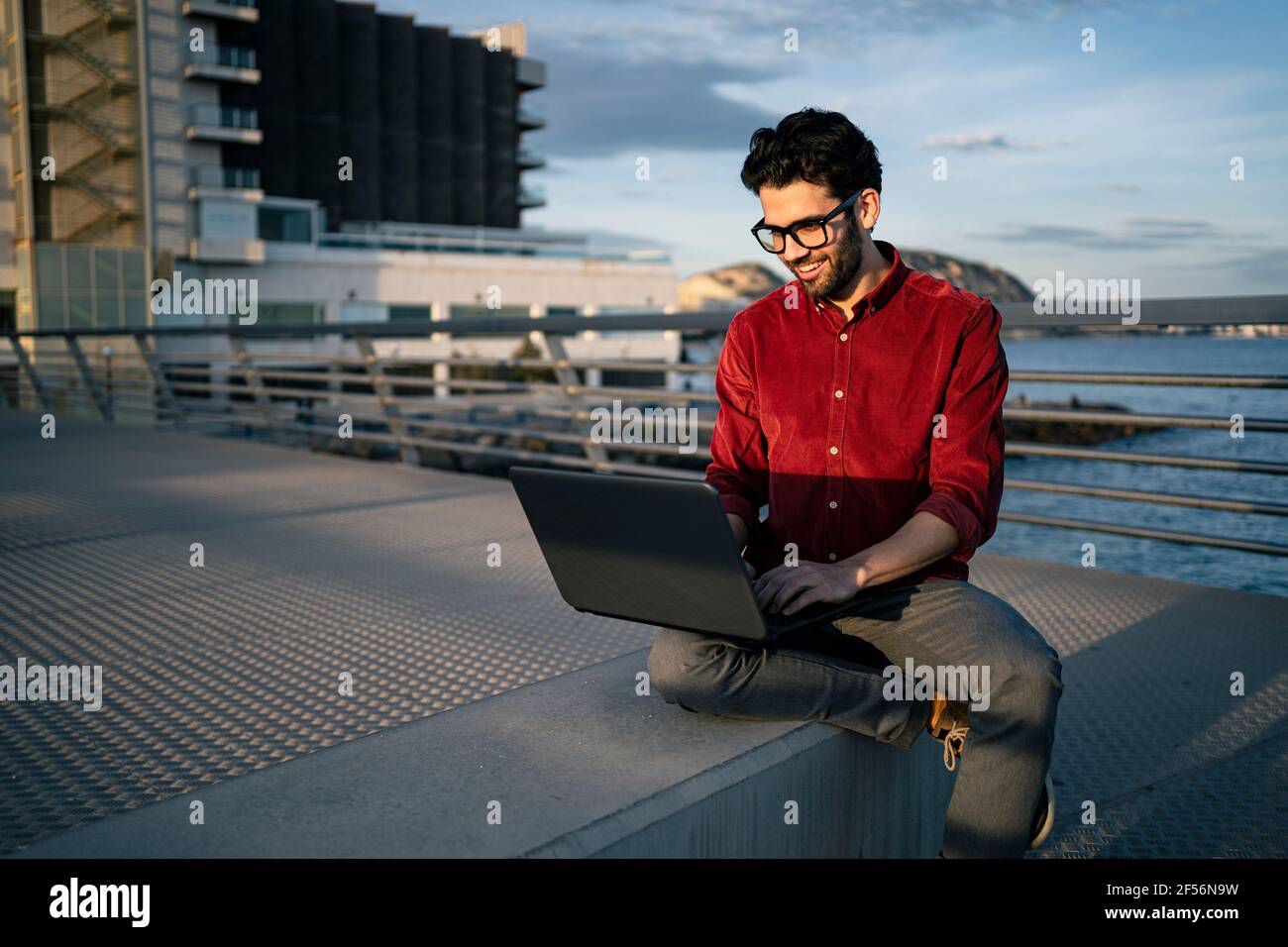 Sorridente lavoratore freelance maschile utilizzando il computer portatile sul banco Foto Stock