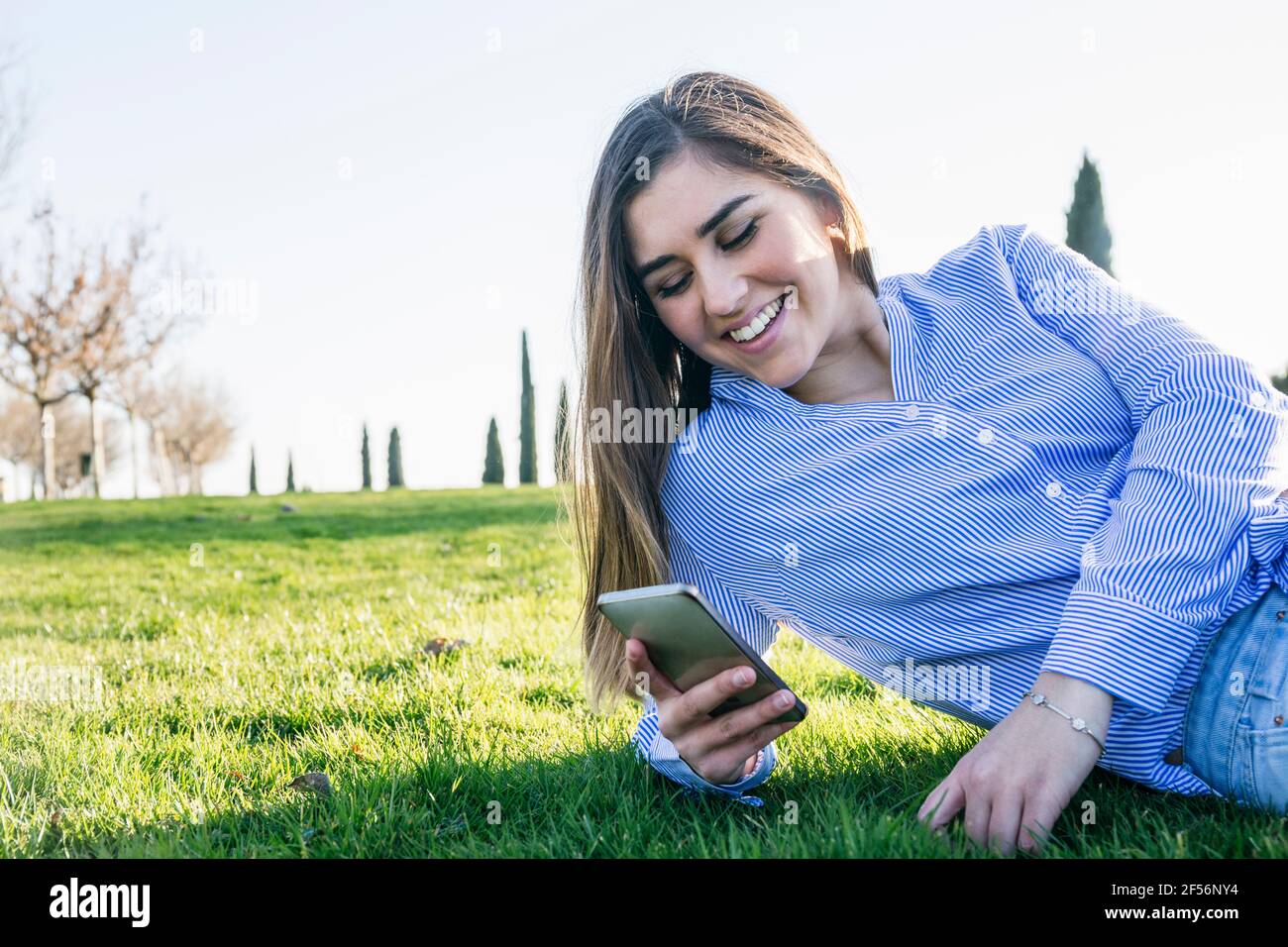 Bella donna che usa lo smartphone mentre si sdraiava a fianco durante giorno di sole Foto Stock