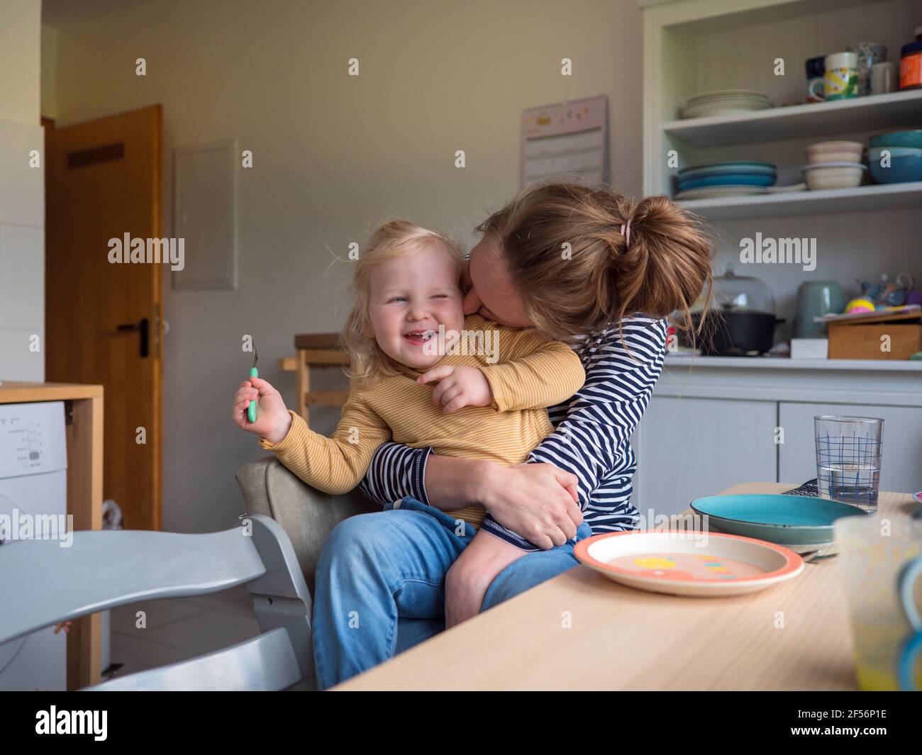 Madre allegra che abbraccia la figlia in cucina a casa Foto Stock