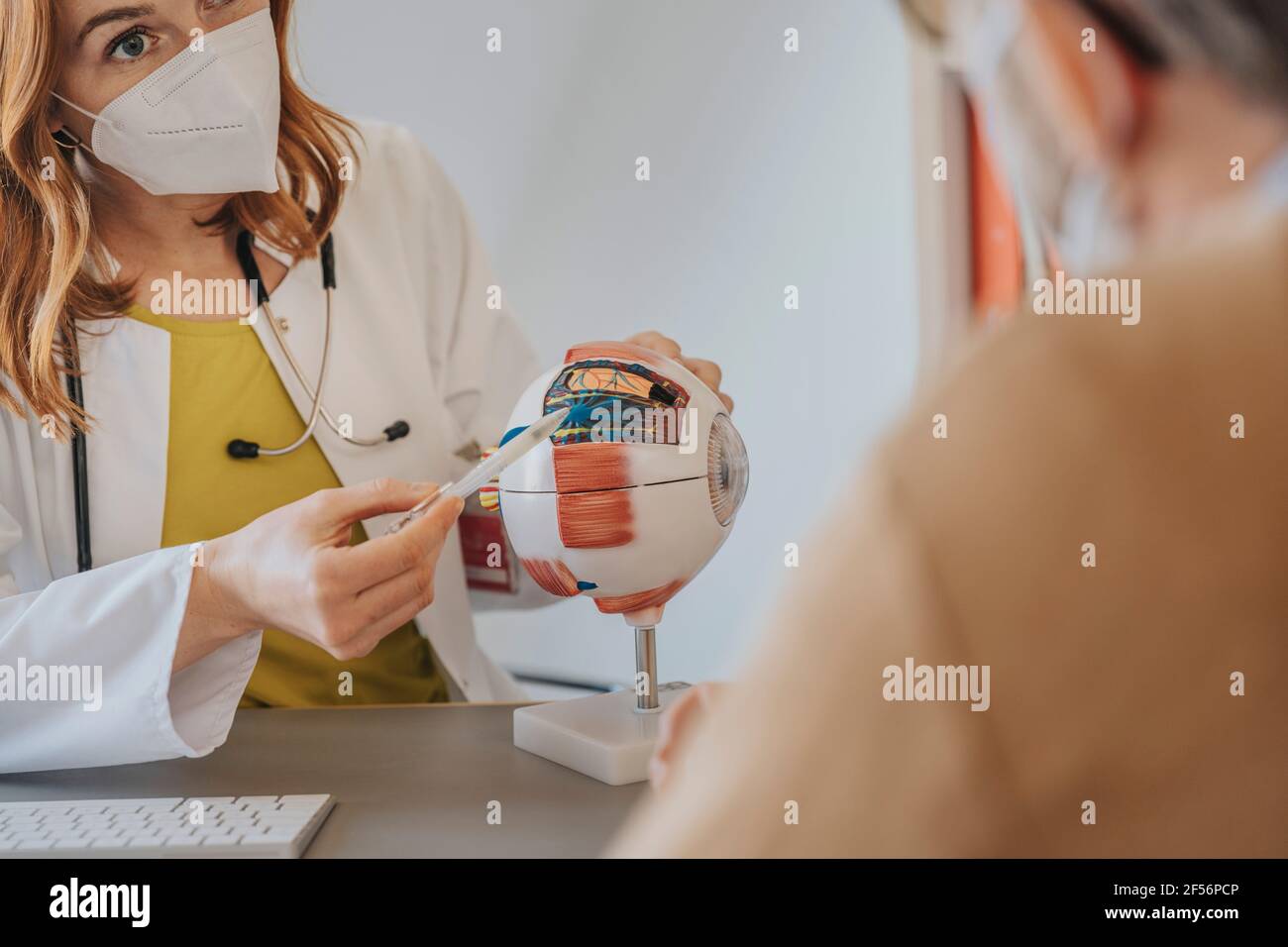 Medico femminile con maschera protettiva che spiega sopra l'occhio artificiale al paziente in clinica Foto Stock
