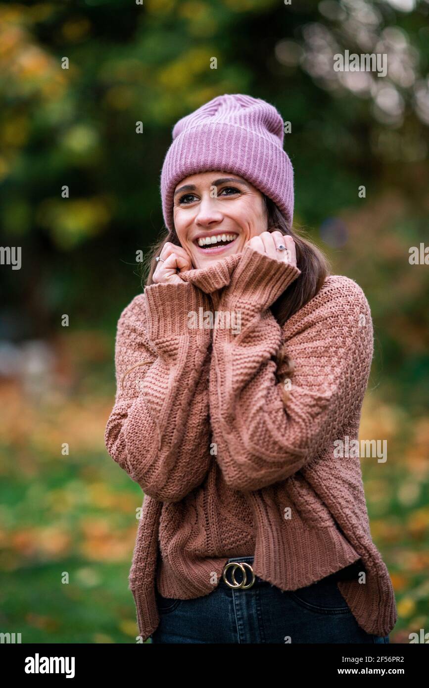 Ritratto di bella donna con cappello e maglione in maglia rosa in piedi all'aperto e sorridente Foto Stock