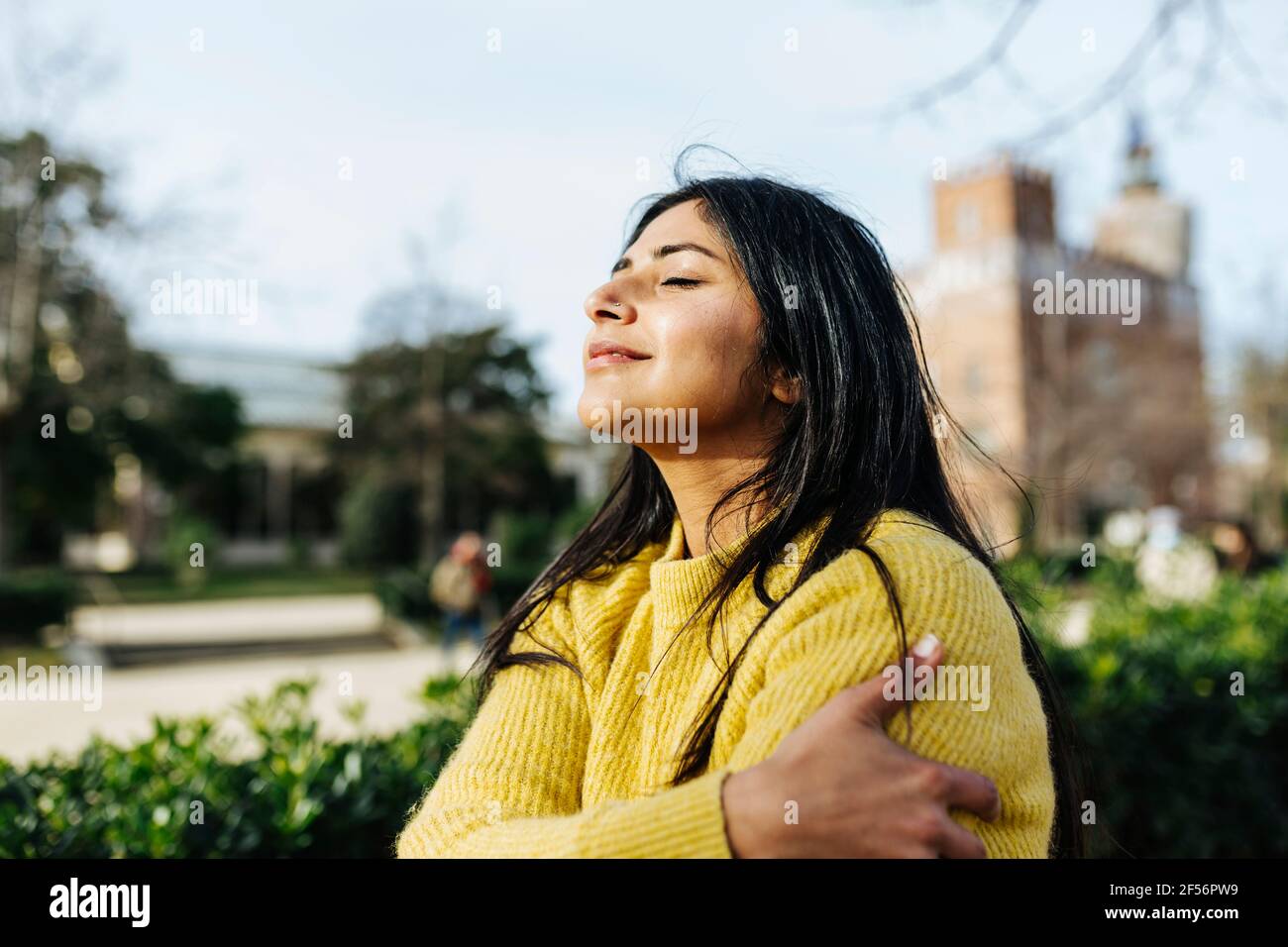 Donna sorridente che si agguantano contro il cielo nel parco pubblico Foto Stock