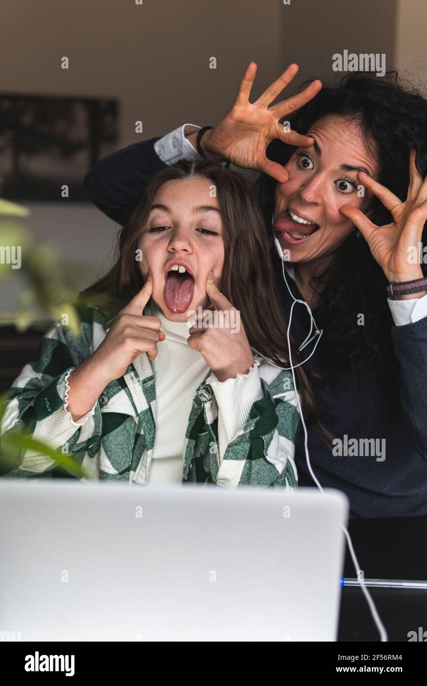 Mamma allegra con figlia che fa i volti davanti al digitale tablet a casa Foto Stock