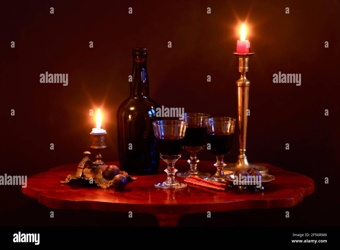 Studio shot di bottiglia di vino rosso, tre verricelli ripieni, prugne, pretzel salati e candele che bruciano in antichi portacandele in piedi su un piccolo tavolino da caffè Foto Stock