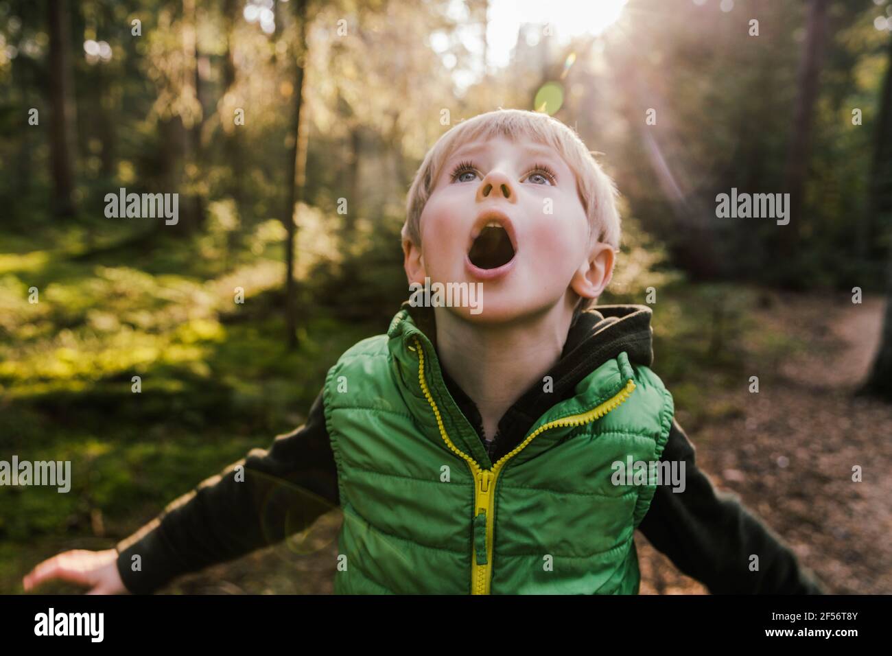 Ragazzo con bocca aperta in piedi in foresta Foto Stock