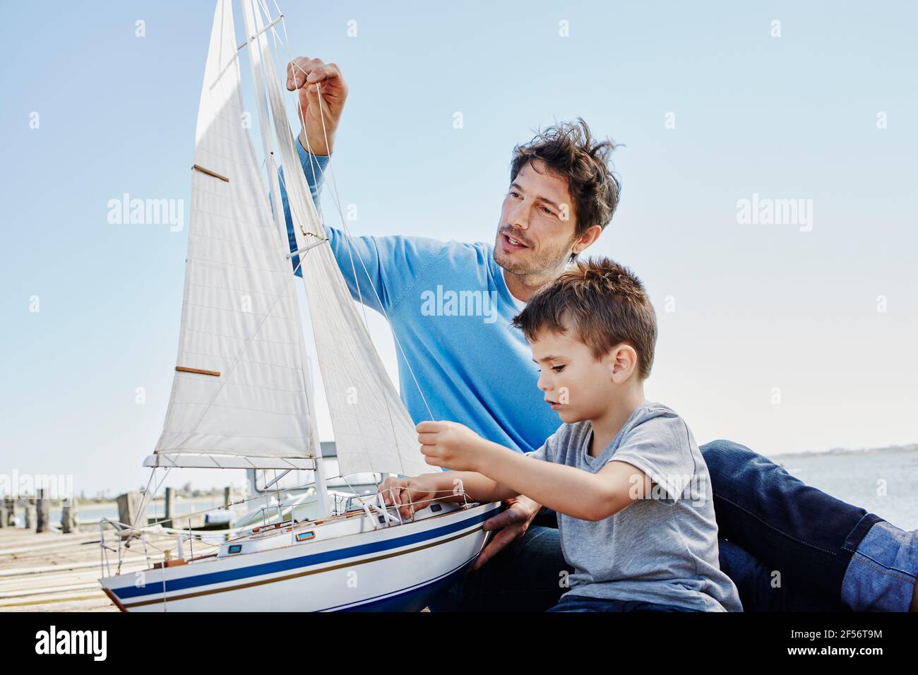 Padre e figlio preparano insieme il giocattolo a vela mentre si siedono molo Foto Stock