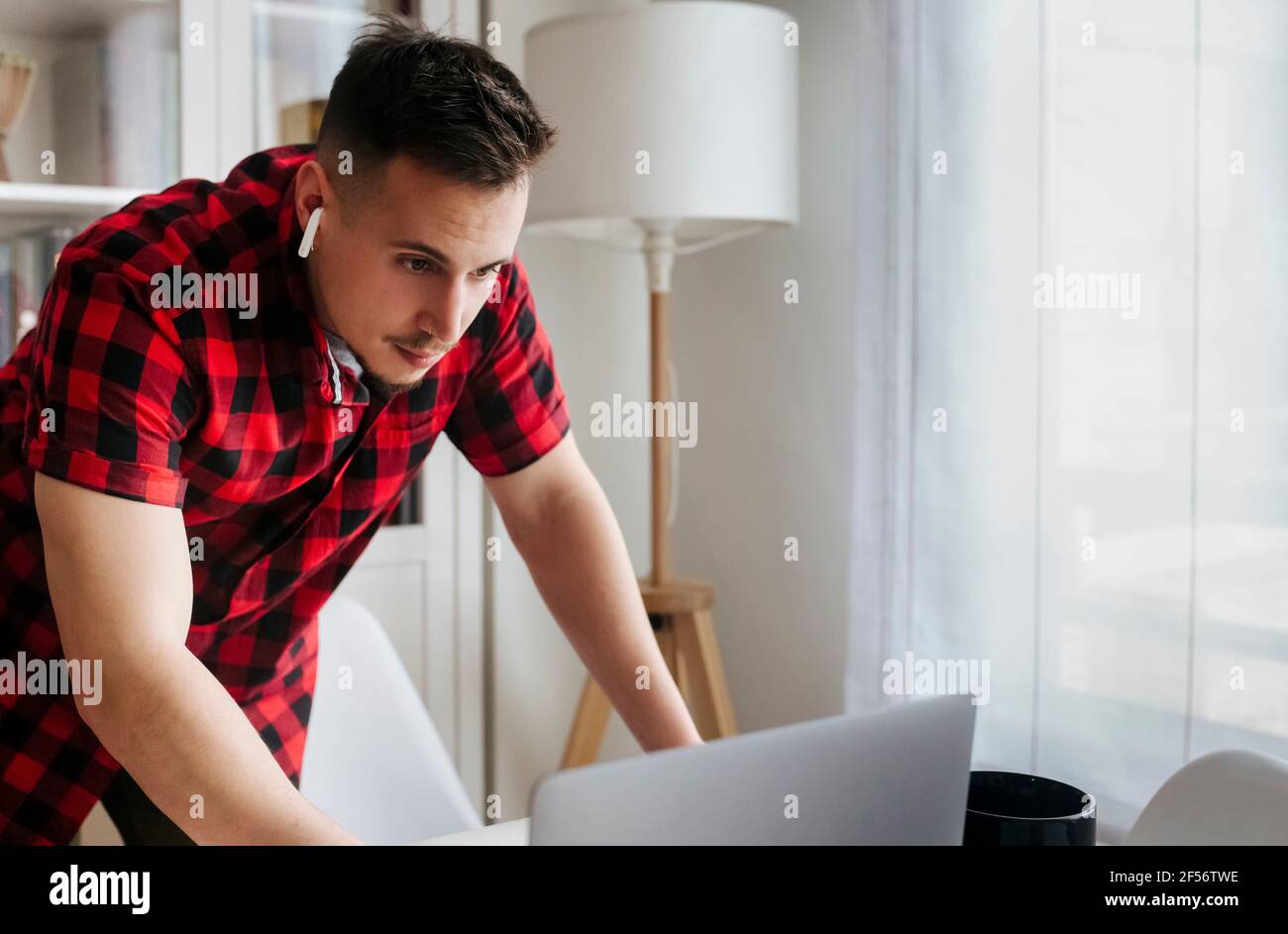 Imprenditore maschile con cuffie intrauricolari appoggiate sul tavolo mentre si utilizza il computer portatile in ufficio Foto Stock