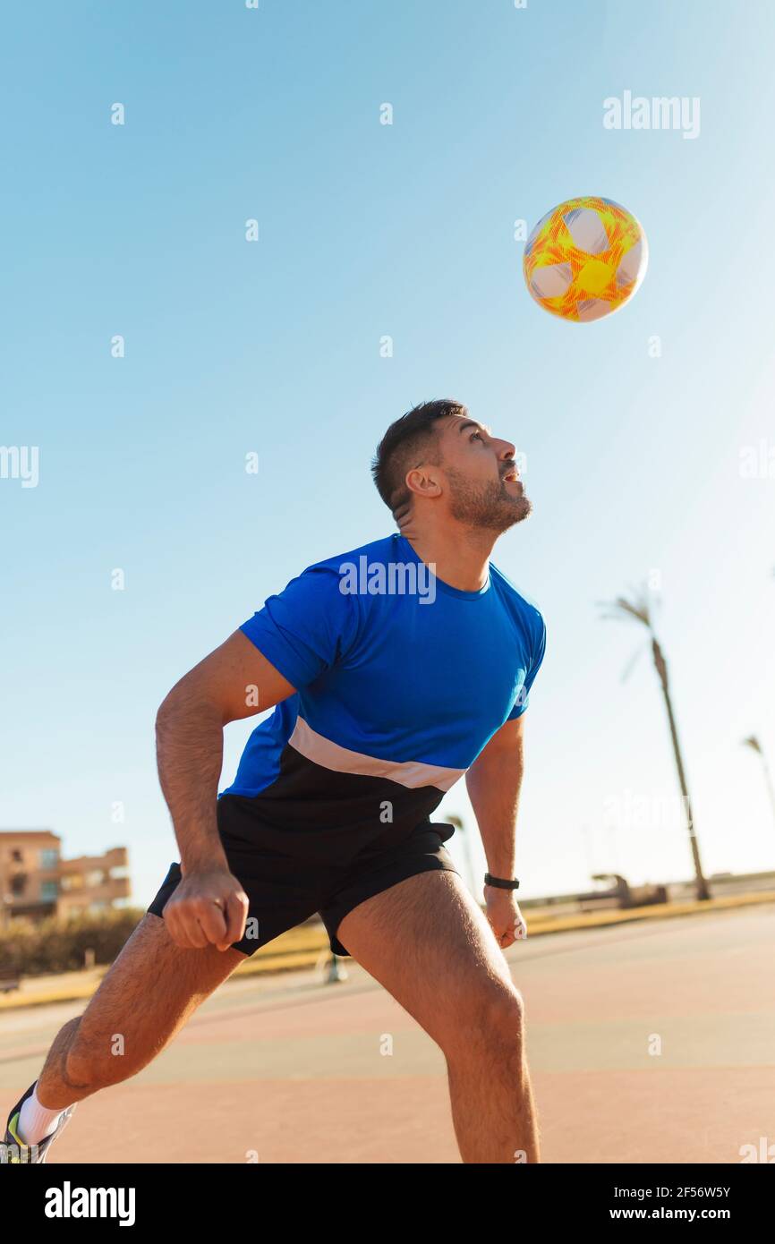 Uomo che dirige la palla mentre gioca a calcio durante la giornata di sole Foto Stock