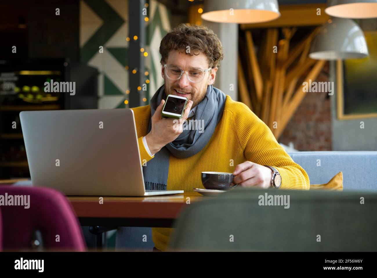 Uomo d'affari che invia messaggi vocali tramite smartphone mentre si ha il caffè al caffè Foto Stock