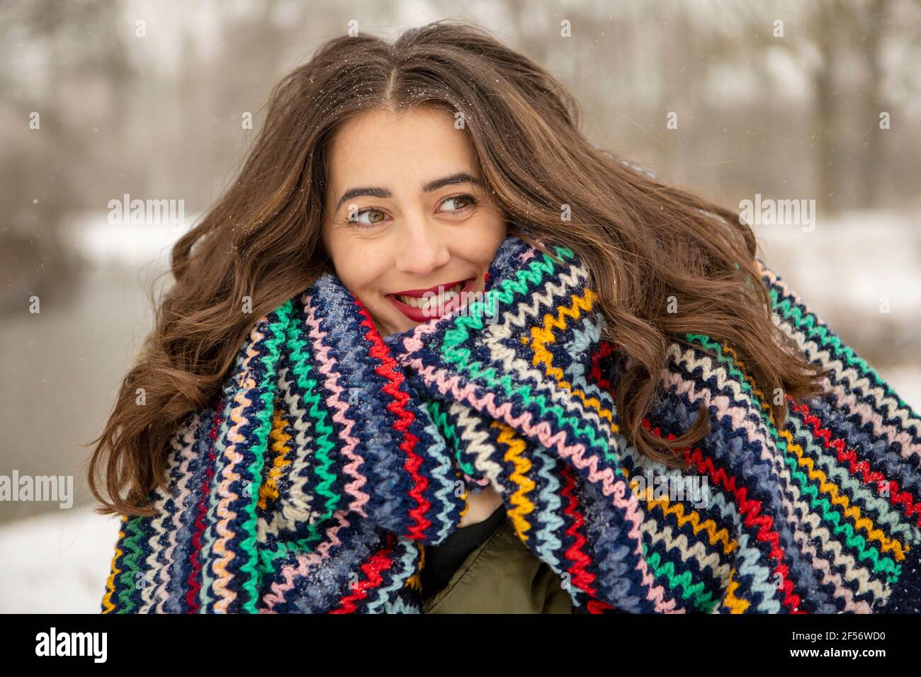 Donna sorridente avvolta in coperta multicolore mentre guarda via durante l'inverno Foto Stock