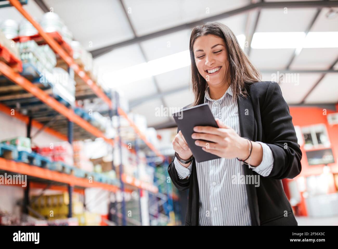 Sorridente manager femminile che utilizza un tablet digitale in un magazzino di distribuzione illuminato Foto Stock