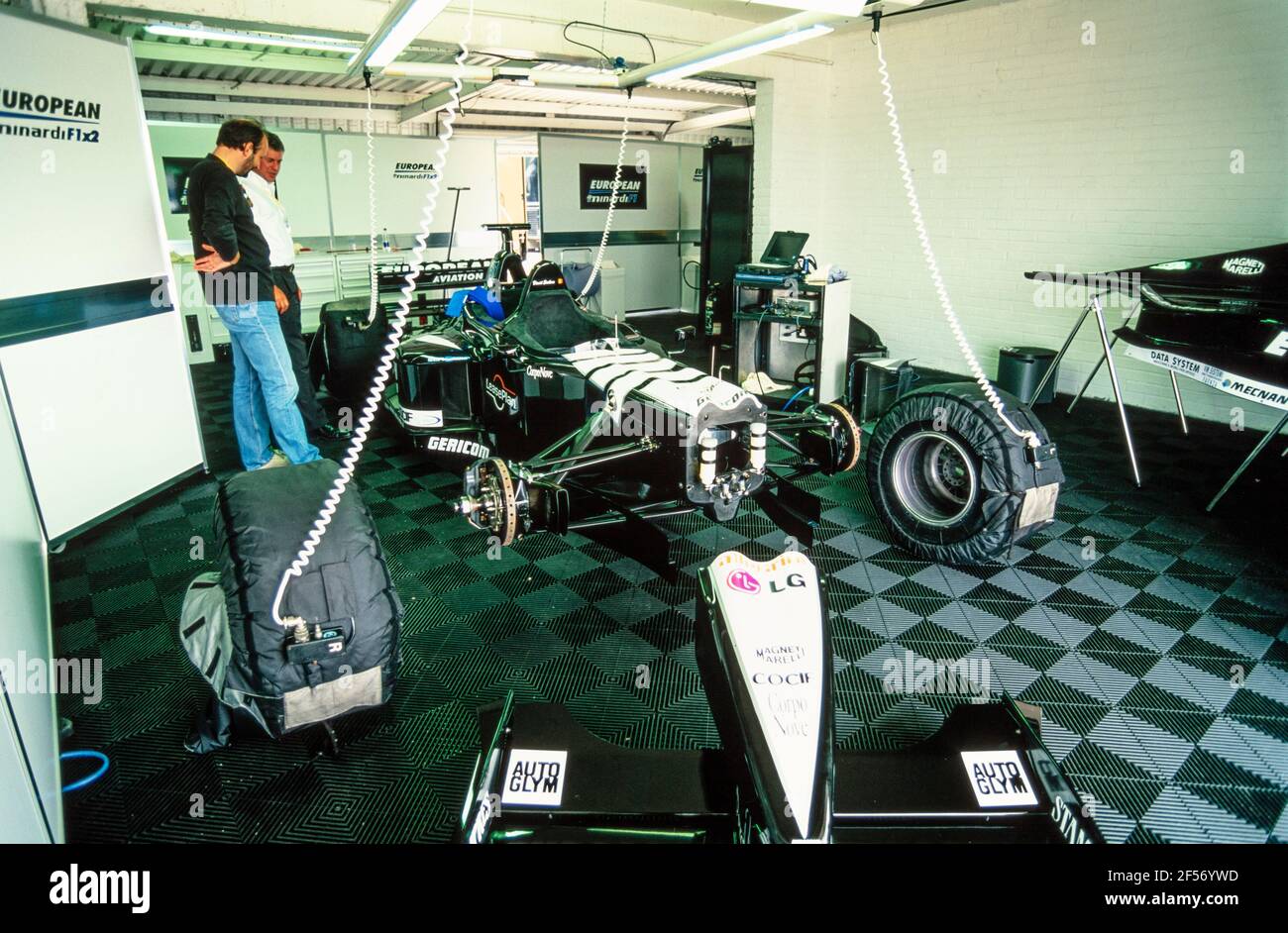 2001 Donington Park Racing Circuit Castle Donington Leicestershire East Midlands England GB UK Europe - due uomini che guardano l'auto europea Minardi V10 a due posti di F1 smantellati nel garage della pit lane in una giornata di esperienza di guida sul circuito di Donington Park. La vettura a 2 posti è una Minardi a 2 posti alimentata dal motore Cosworth V10 da 750 CV e con il cono anteriore rimosso. Si tratta di un'auto Minardi F1x2. Foto Stock