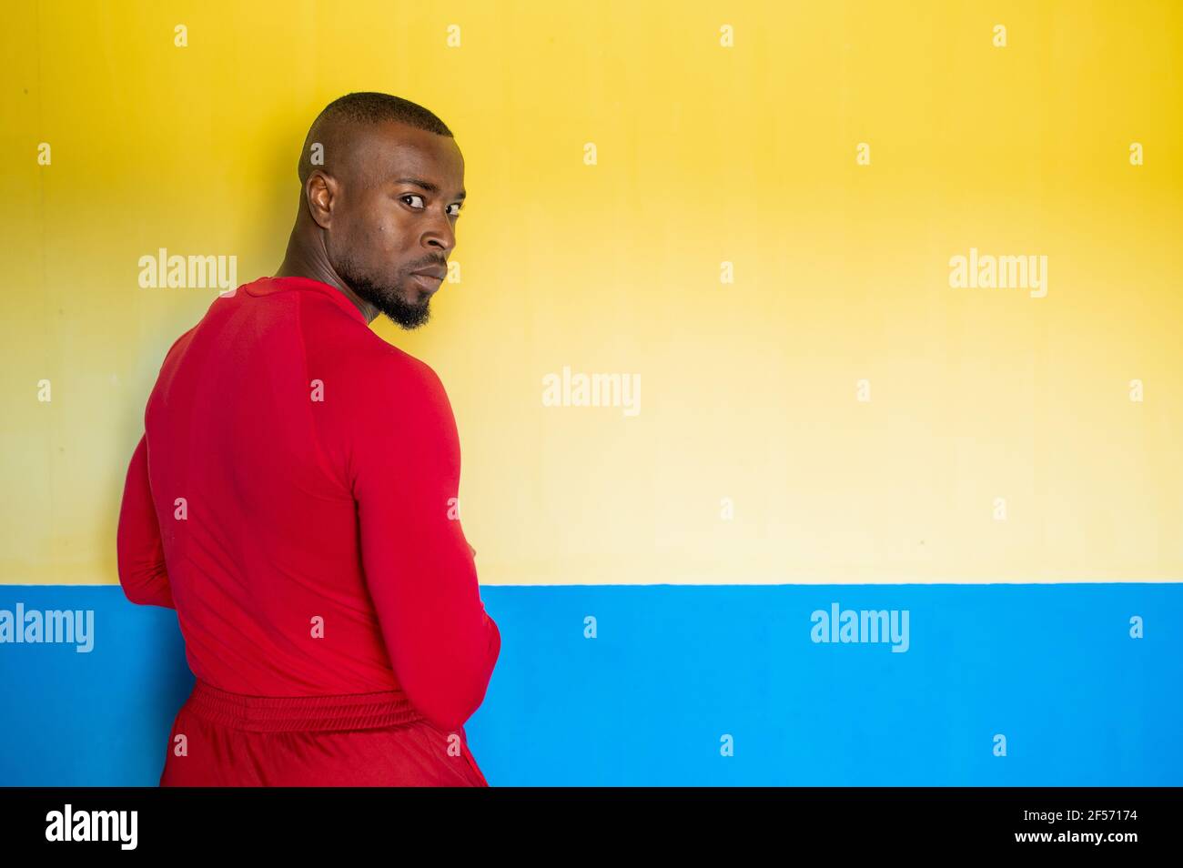 Retro di un uomo sportivo africano con corpo perfetto in piedi davanti a uno sfondo colorato gira la testa per guardare la fotocamera. Foto Stock
