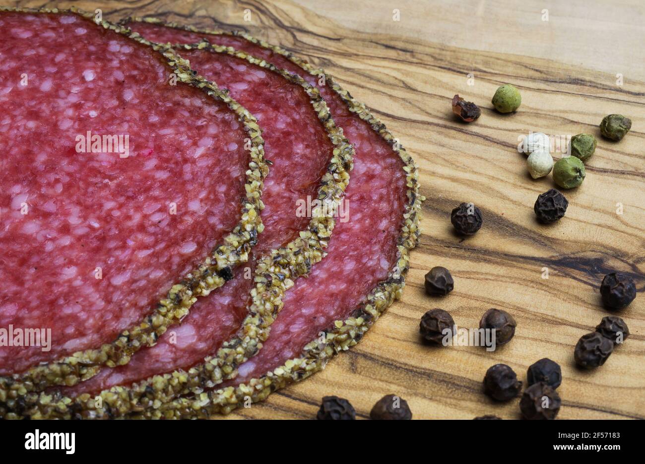 Makro closeup di fette isolate salame francese fresco con misto crosta di pepe e pepe su tagliere di legno d'oliva Foto Stock
