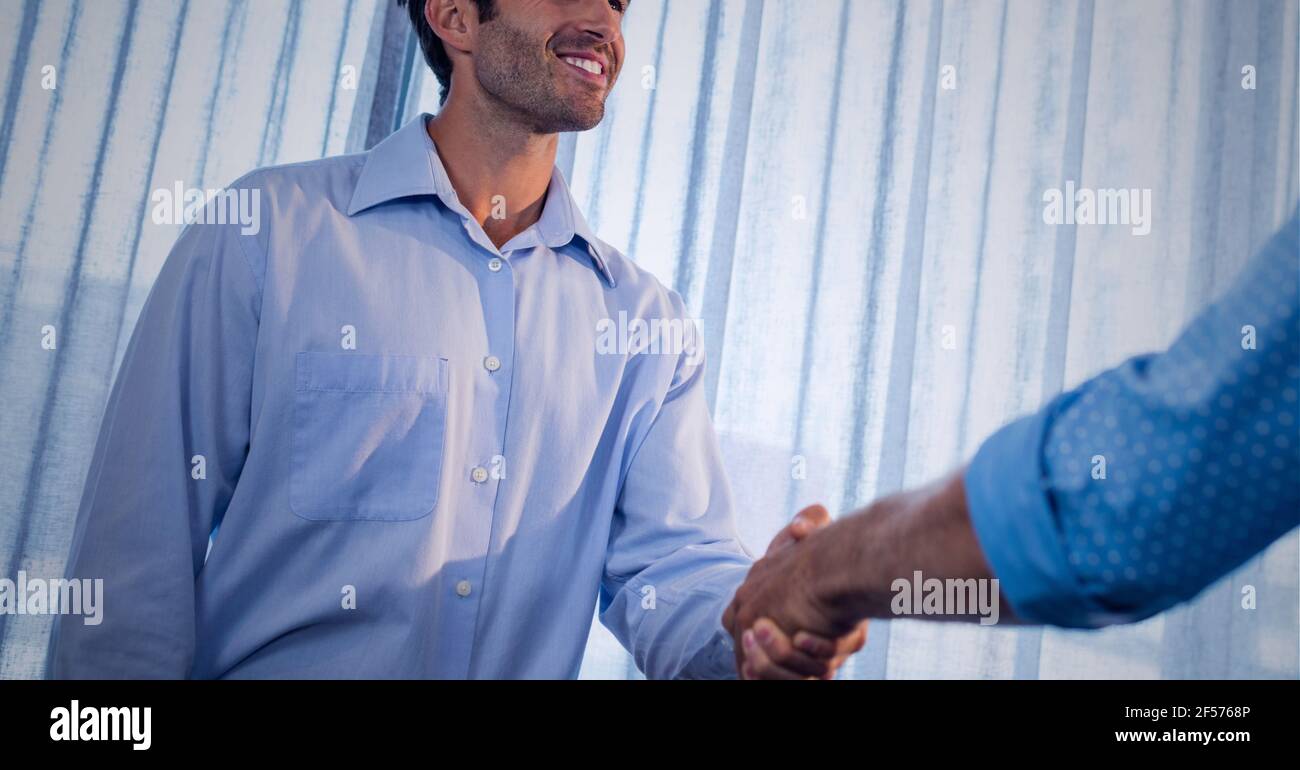 Uomini d'affari che sorridono e scuotono le mani in ufficio Foto Stock