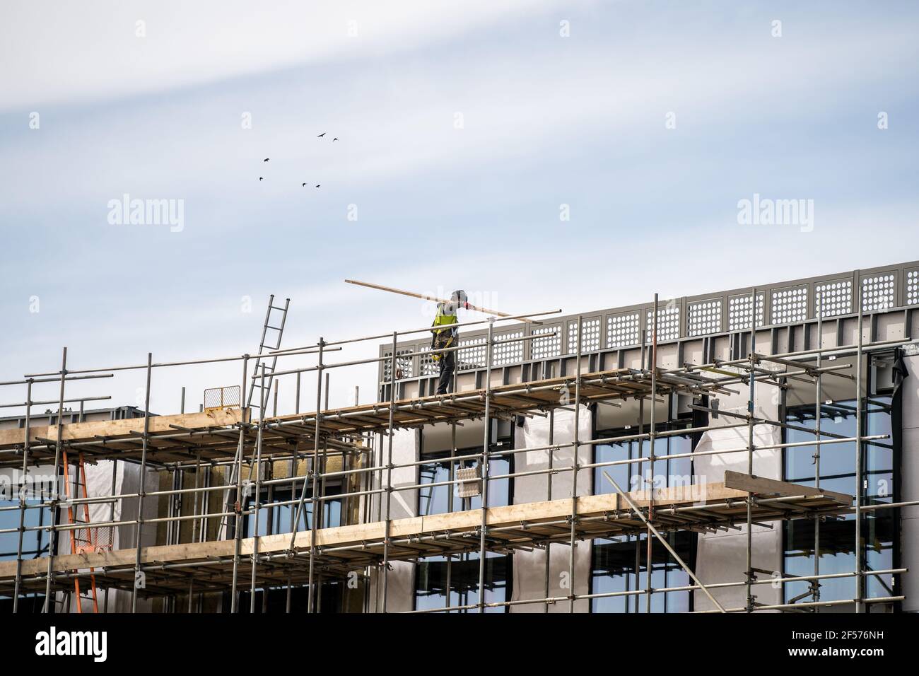 Impalcatura in DPI che erigono il telaio di tavole di legno e alti pali di impalcatura in alto sul nuovo cantiere di costruzione moderna. Pericolo professionale Foto Stock