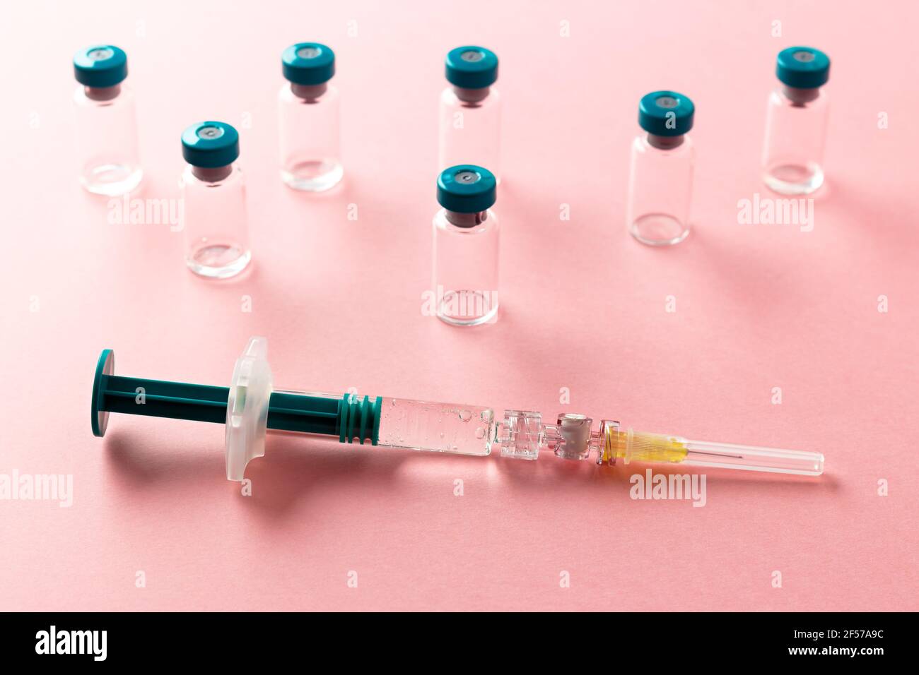 Siringa con diversi flaconcini medici per l'iniezione su sfondo rosa. Foto Stock