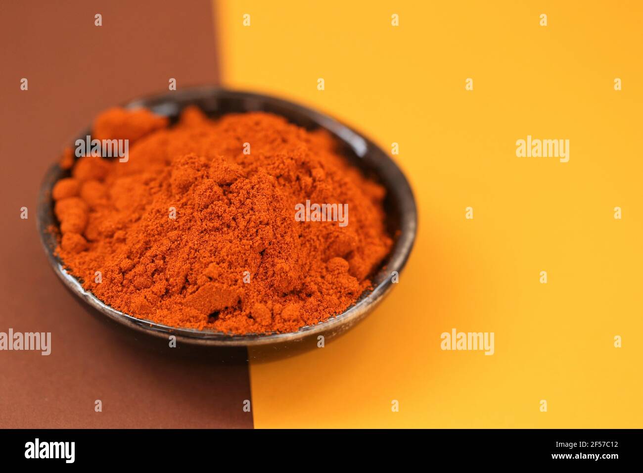 Pepe rosso in polvere. Pepe caldo. Spezie e condimenti concetto peperoni rossi in un piatto di ceramica nera su un marrone e giallo combinato background.Food e. Foto Stock