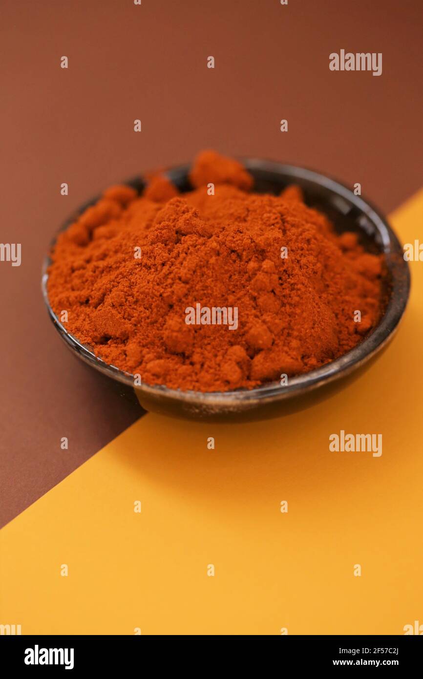 Pepe rosso in polvere. Pepe caldo. Spezie e condimenti. Peperoni rossi in un piatto nero di ceramica su un marrone e giallo combinato background.Food e cucina Foto Stock