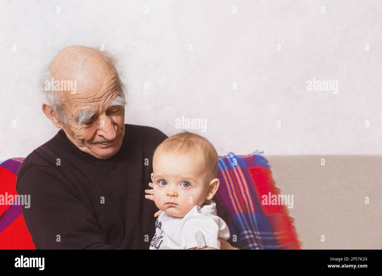 Nonno anziano con nipote seduto sul divano. Uomo che parla con suo nipote. Bisnonno e bisnonno. Nonno sta guardando al bambino. Foto Stock