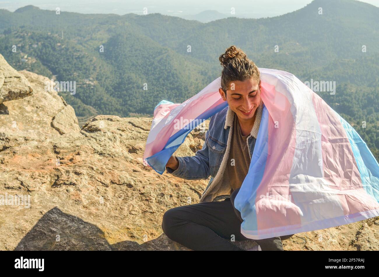 Giovane spagnolo con la bandiera trans sulle spalle su una cima di una montagna Foto Stock