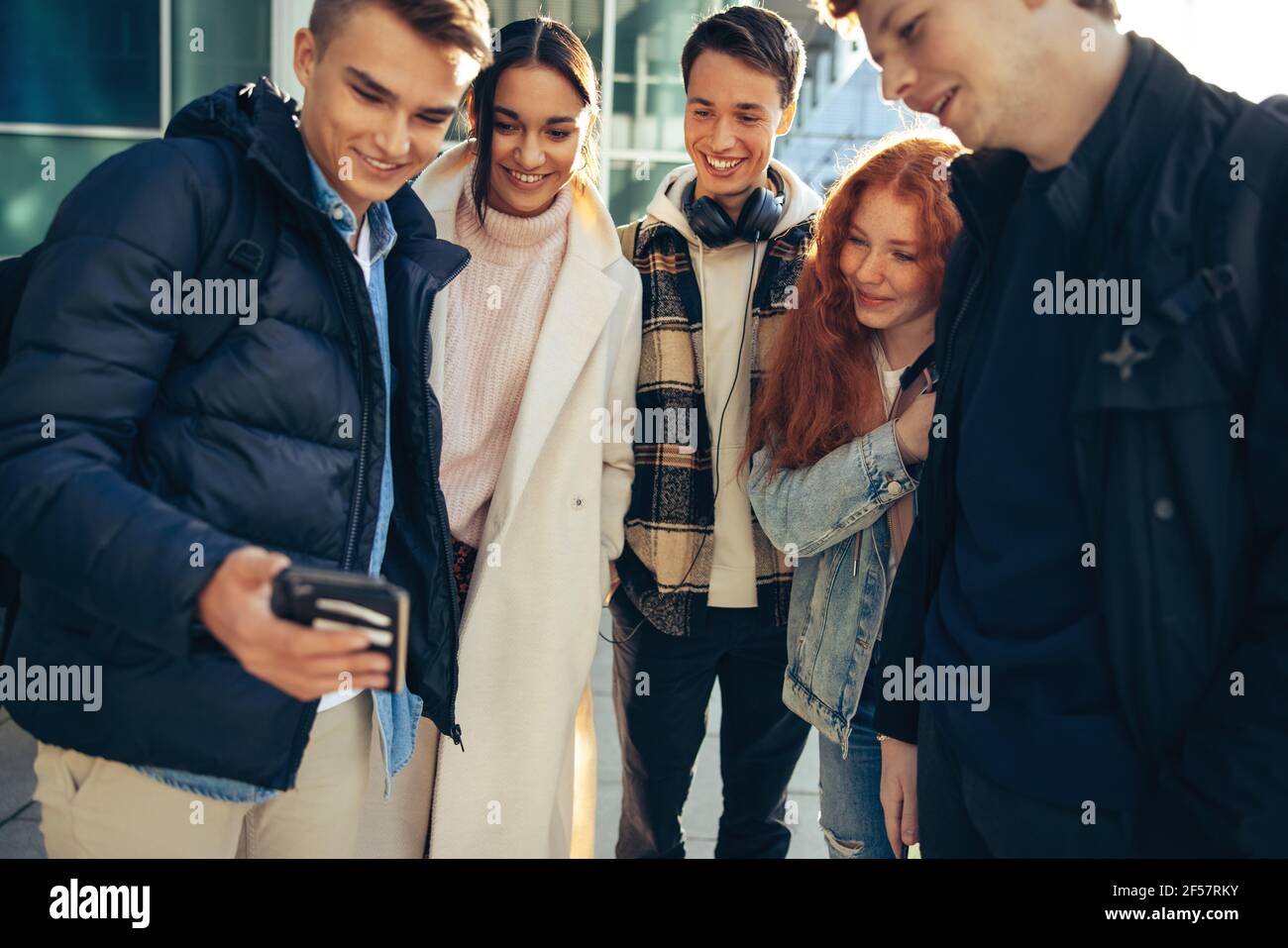 Gruppo di amici che guardano un cellulare. studenti universitari all'aperto che usano il telefono. Foto Stock
