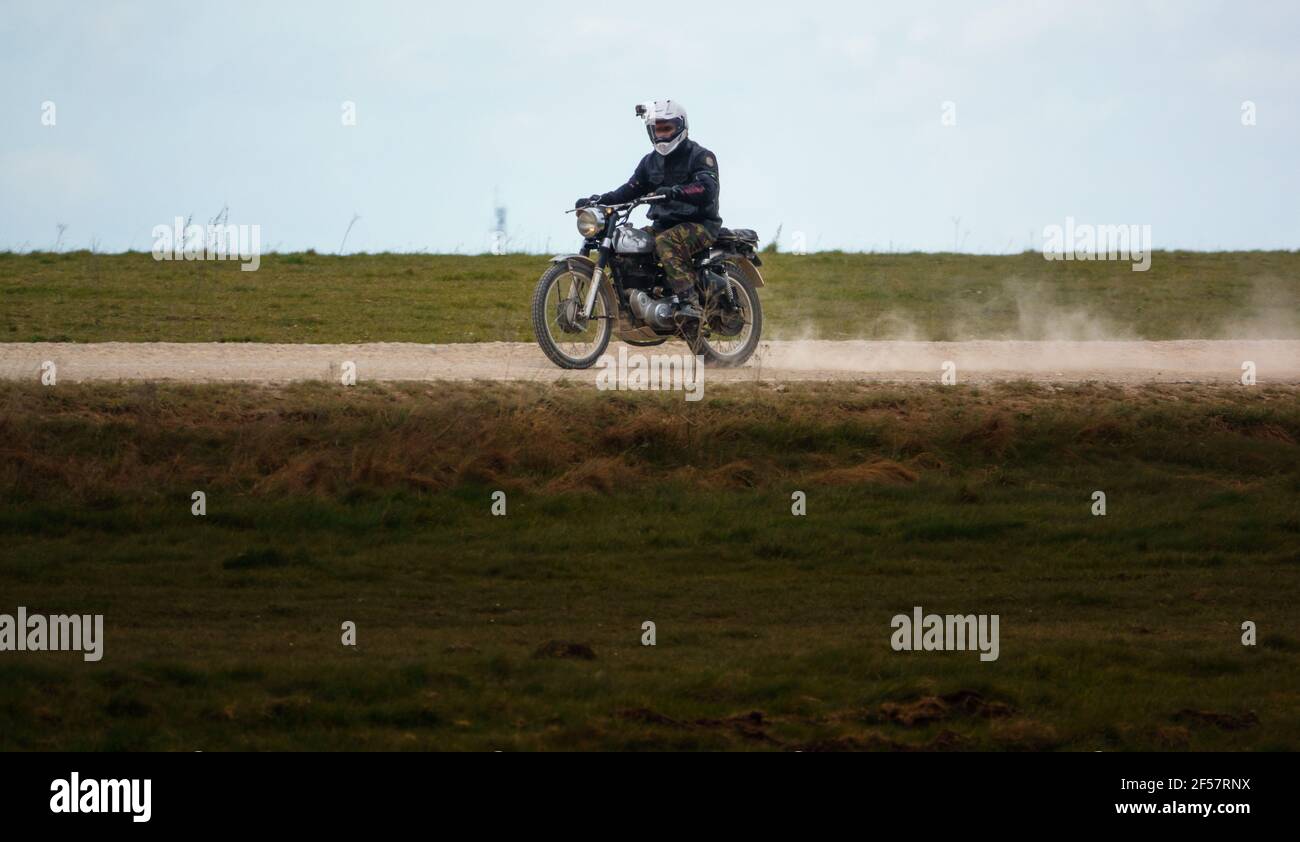 Un motociclista guida la sua classica moto reale Enfield a quattro tempi Lungo una polverosa pista di pietra sopra Salisbury Plain Foto Stock