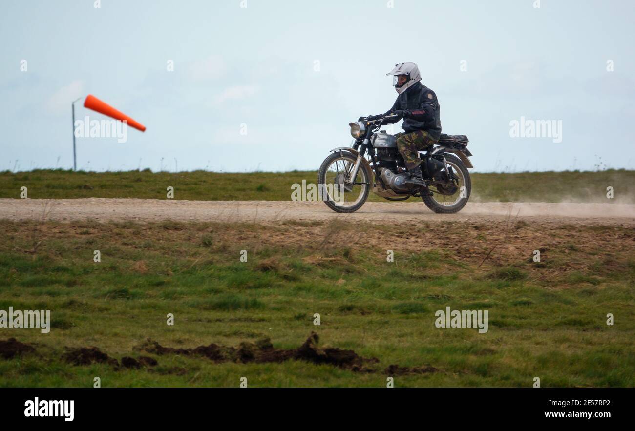 Un motociclista guida la sua classica moto reale Enfield a quattro tempi Lungo una polverosa pista di pietra sopra Salisbury Plain Foto Stock