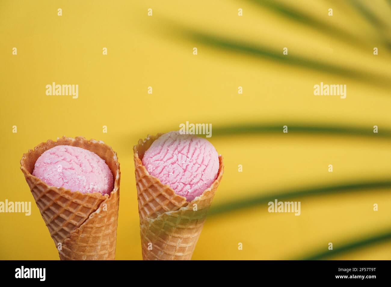 Due gelati alla fragola in un cono su sfondo giallo. Foglia tropicale Foto Stock